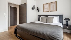 A modern bedroom with a dark wood bed, a bedside table with a lamp, and two abstract wall art pieces.