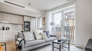 A modern apartment with a grey sofa, a coffee table, and a kitchen in the background.