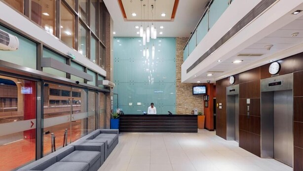 A modern hotel lobby with a reception desk, seating area, and elevators. - Double Room Near Abu Shagara Park by E R (Sharjah)