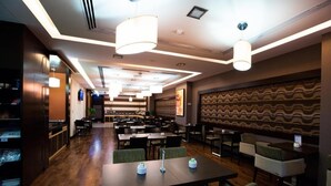 A spacious restaurant with multiple dining tables and chairs, modern pendant lighting, and a patterned wall design. - Double Room Near Abu Shagara Park by E R (Sharjah)