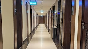 A long, narrow hallway with a polished marble floor, wooden paneling on the walls, and a series of doors on one side.