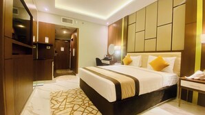 A modern hotel room with a large bed, a bedside table, a mirror, and a wardrobe.