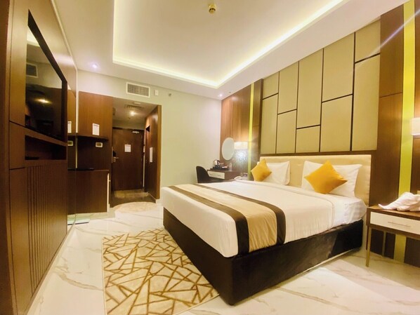 A modern hotel room with a large bed, a bedside table, a mirror, and a wardrobe.