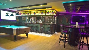 A billiards table, bar area, and seating arrangement in a room with wooden flooring and decorative wall panels.