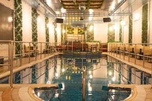 An indoor swimming pool with a central diving platform, surrounded by seating areas and walls adorned with greenery. - Superior Room Near Go Fresh Supermarket by E R (Dubai)