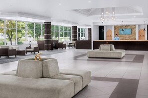 A spacious lobby with a reception desk, seating areas, and large windows offering views of the outdoors.