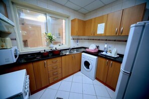 Une cuisine compacte avec des meubles en bois, un lave-linge, un four à micro-ondes et une fenêtre agrémentée d’une plante.