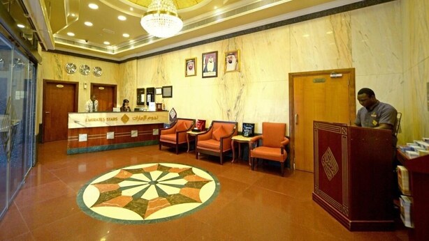 A hotel lobby with a reception desk, seating area, and a large decorative floor design. - Studio Apartment Near Al Khan Beach By E R (الشارقة)