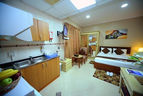 Une chambre d’hôtel comprenant un lit, un bureau, une chaise, une petite table, un téléviseur et un coin cuisine avec un évier et des placards.