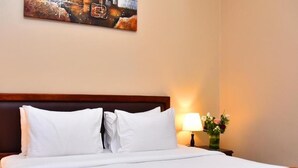A hotel room with a neatly made bed, a wooden headboard, a bedside table with a lamp, and a wall-mounted painting. - Studio Apartment Near Al Khan Beach By E R (الشارقة)