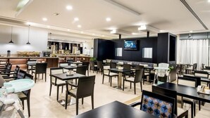 A spacious restaurant with multiple tables and chairs, a bar area, and a television screen.