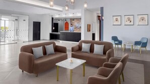 A modern hotel lobby with two sofas, a reception desk, and framed artwork on the wall.