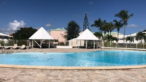 A swimming pool with white gazebos, palm trees, and a stone-tiled deck. - JUST A LITTLE BIT  (Saint-François)