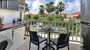 A balcony with a view of palm trees and houses, a washing machine, and a table with chairs. - JUST A LITTLE BIT  (Saint-François)