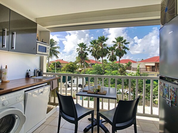A balcony with a view of palm trees and houses, a washing machine, and a table with chairs. - JUST A LITTLE BIT (Saint-François)