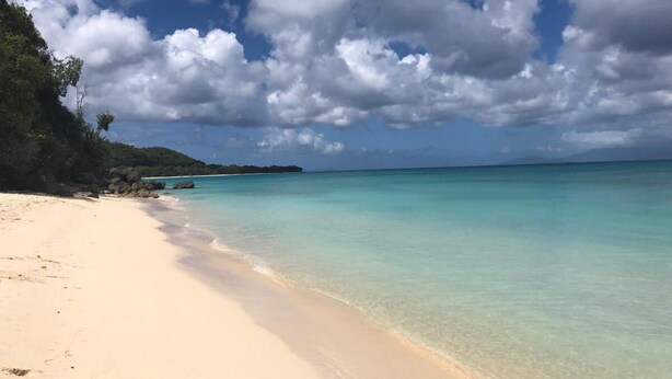 A beach with clear turquoise water, a sandy shore, and a hilly landscape in the background. - JUST A LITTLE BIT  (Saint-François)