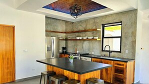 A modern kitchen with a large island, bar stools, a refrigerator, and a window providing natural light.