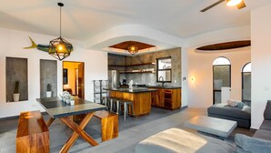 A modern kitchen with a central island, bar stools, and a dining table with wooden legs.