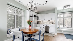 A modern kitchen with white cabinets, a central island with chairs, and a dining table. - The Shores Lake View Condo Unit 5689 (Williamsburg)