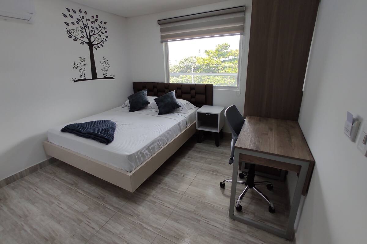 Quarto com cama, mesa de cabeceira e escrivaninha com cadeira.