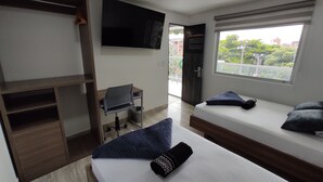 A hotel room with a bed, a desk, a chair, a TV, and a window with a view of buildings and trees. - Cra. 81 No. 37d - 17 (Medellín)