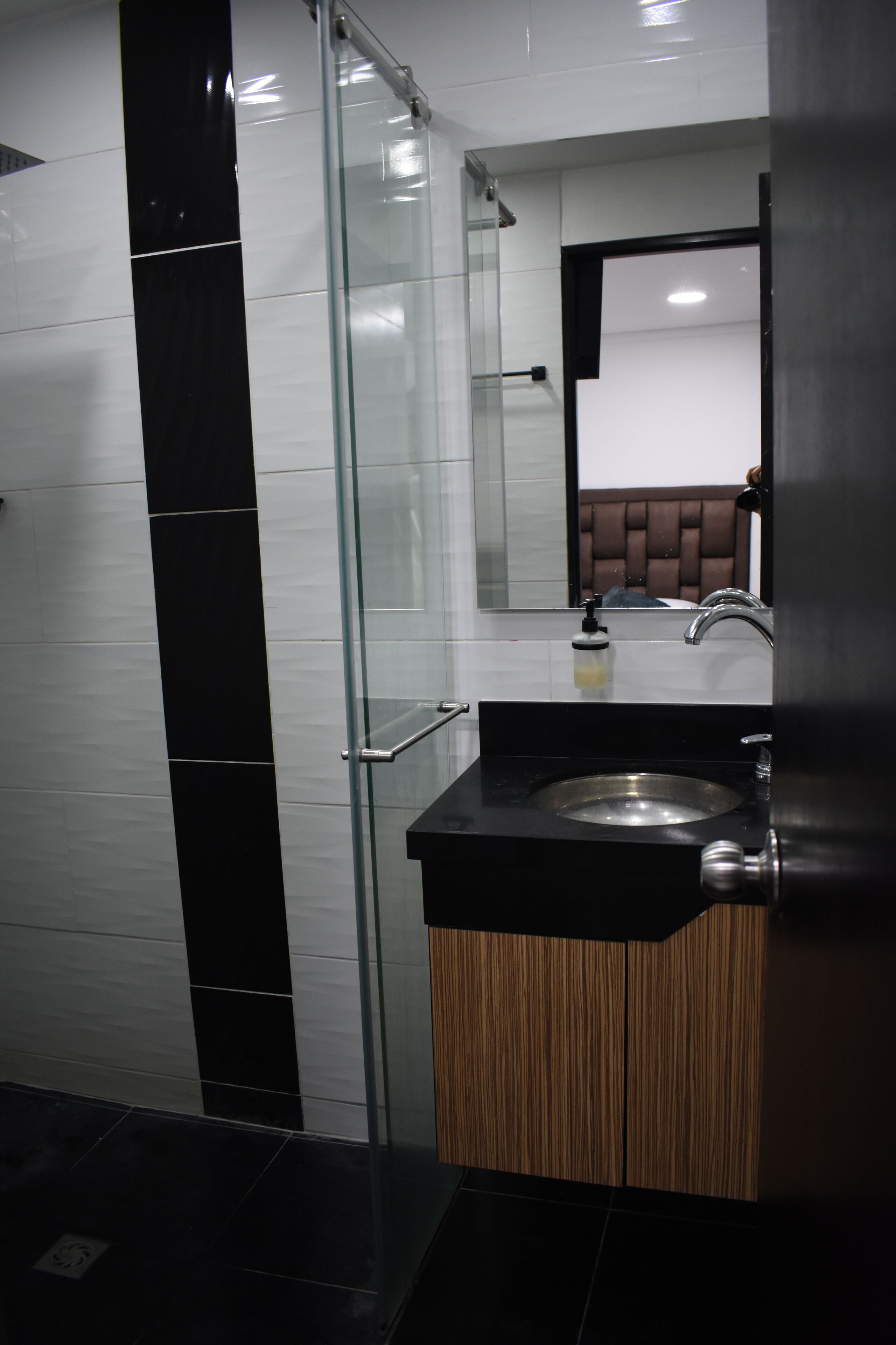 Un baño moderno con cabina de ducha de vidrio, un lavabo negro y un mueble de madera.