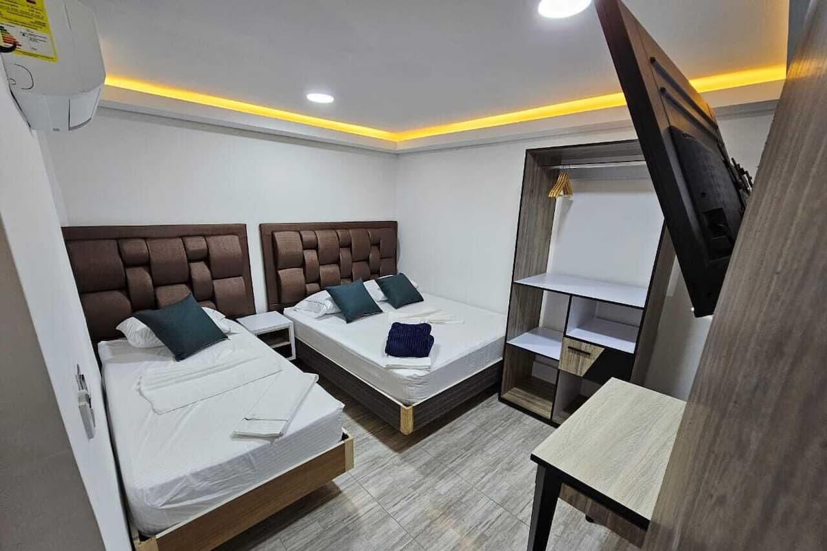 Quarto de hotel com duas camas, uma mesa e uma televisão.