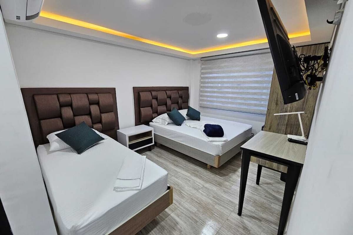 Quarto de hotel moderno com duas camas, uma escrivaninha e uma televisão.