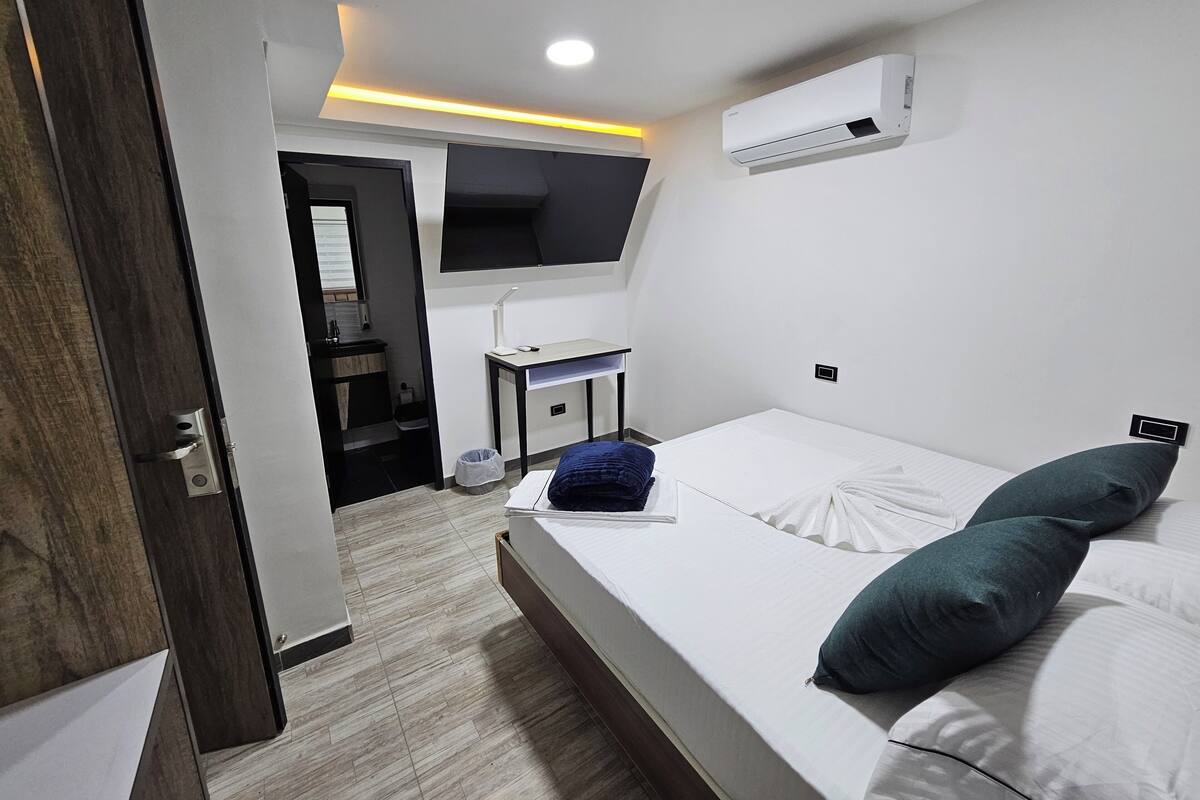 Quarto de hotel moderno com uma cama grande, uma escrivaninha e televisão montada.