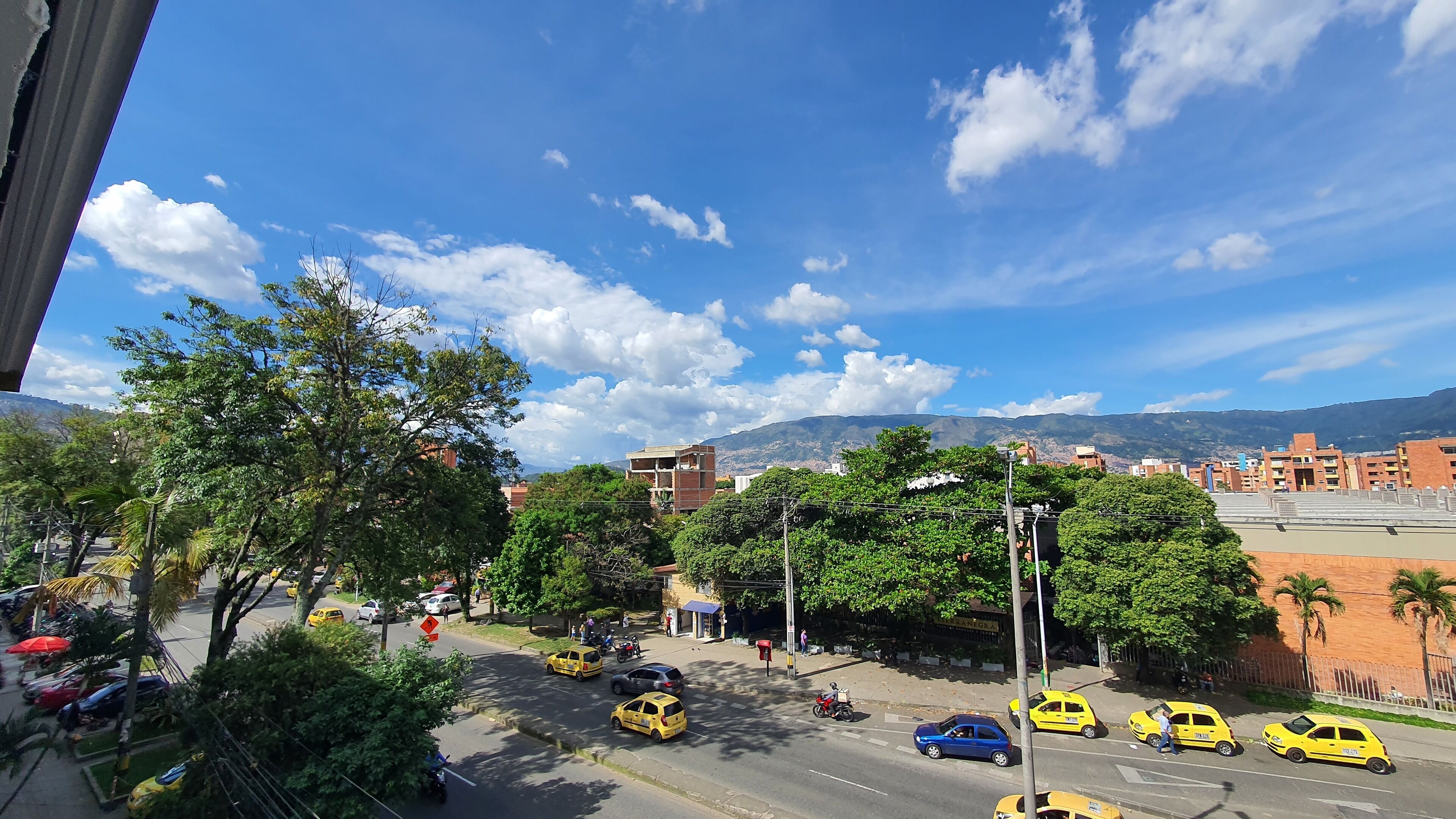 Vista de una calle con taxis amarillos, un cielo azul despejado y edificios al fondo.