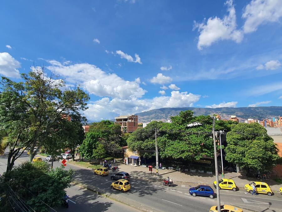 Vista de una calle con taxis amarillos, un cielo azul despejado y edificios al fondo.