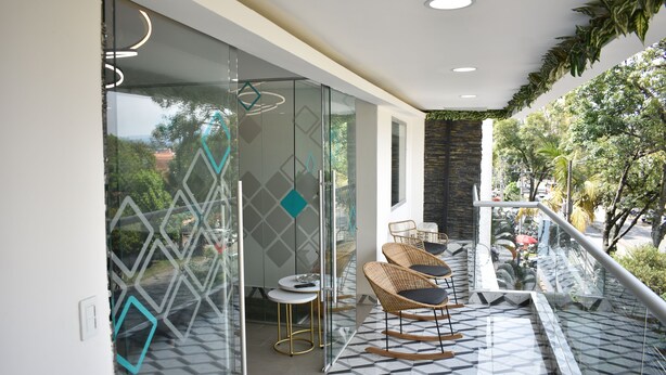 A modern interior with glass partitions, a geometric patterned floor, wicker chairs, and a balcony with a view of greenery. - Cra. 81 No. 37d - 17 (Medellín)