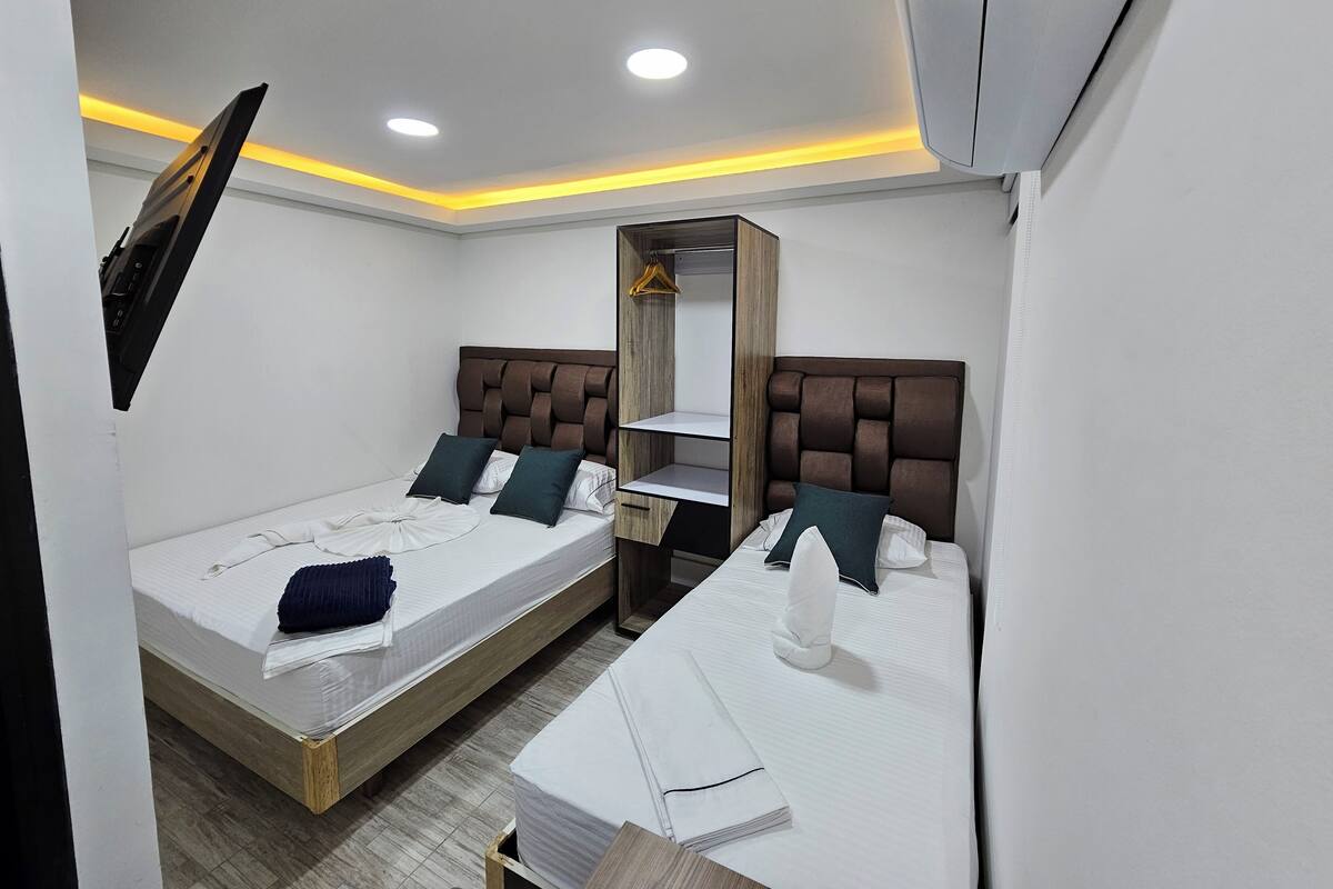 Quarto de hotel compacto com duas camas, um guarda-roupa, um espelho e ar condicionado no teto.