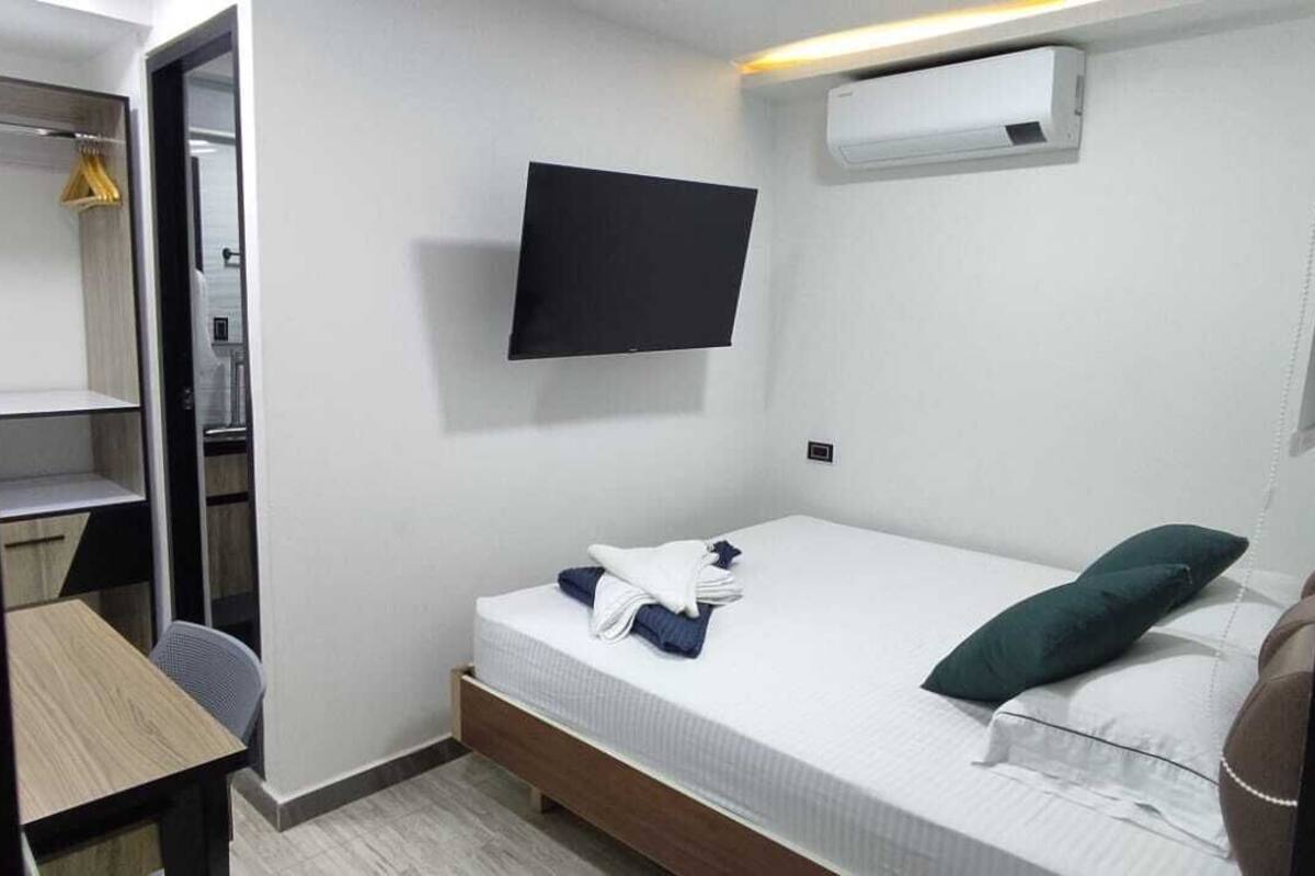 Quarto compacto com cama, escrivaninha, cadeira, televisão e armário.