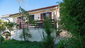 A two-story house with a balcony, surrounded by lush greenery. - Cottage - Sleeps 4 - Parking - Garden (Noto)