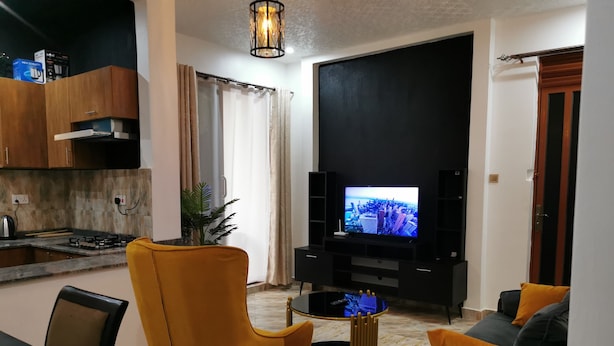 Una sala de estar moderna con un televisor de pantalla plana, un comedor con una mesa y sillas, y una cocina con estufa a gas.