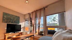 A modern living room with a flat-screen TV, wooden furniture, and large windows with curtains. - Modern 1BR w/ Balcony | 10 Mins Walk to BC Place & Rogers Arena (Vancouver)