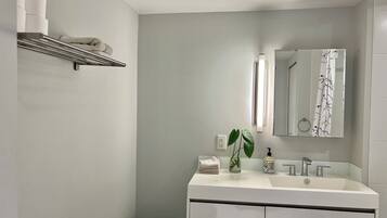 A modern bathroom with a white sink, mirror, and toilet. There is a shelf with towels and a basket.