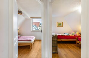 Un corridoio stretto conduce a due camere da letto con pavimento in legno, una finestra con vista sugli edifici e un quadro appeso al muro.