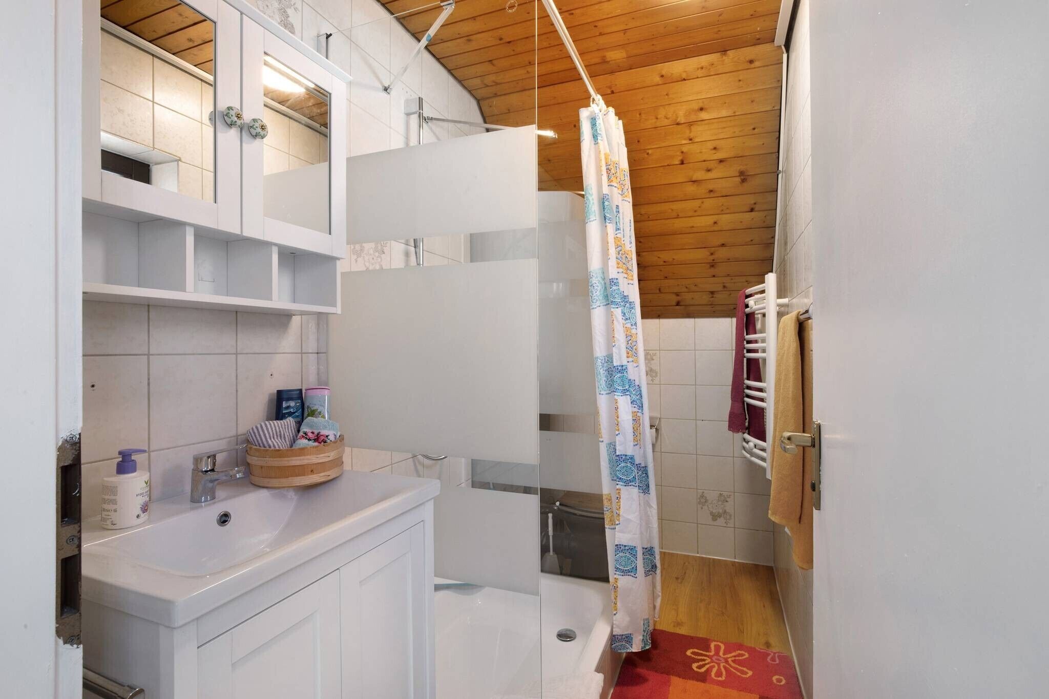 Een badkamer met een wit wastafel, spiegel en planken, een douchegordijn en een handdoekrek.