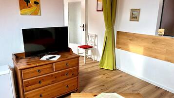Une pièce comprenant une commode en bois, un téléviseur, un lit avec une courtepointe, une porte et un tableau accroché au mur.