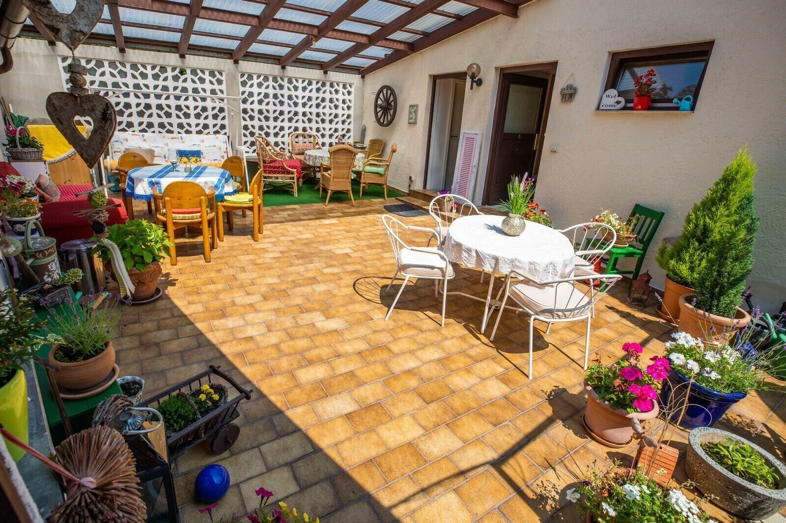 Une terrasse couverte avec un sol en briques, des meubles d’extérieur et des plantes en pot.
