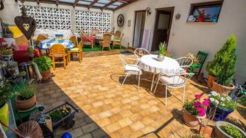 Une terrasse couverte avec un sol en briques, des meubles d’extérieur et des plantes en pot.