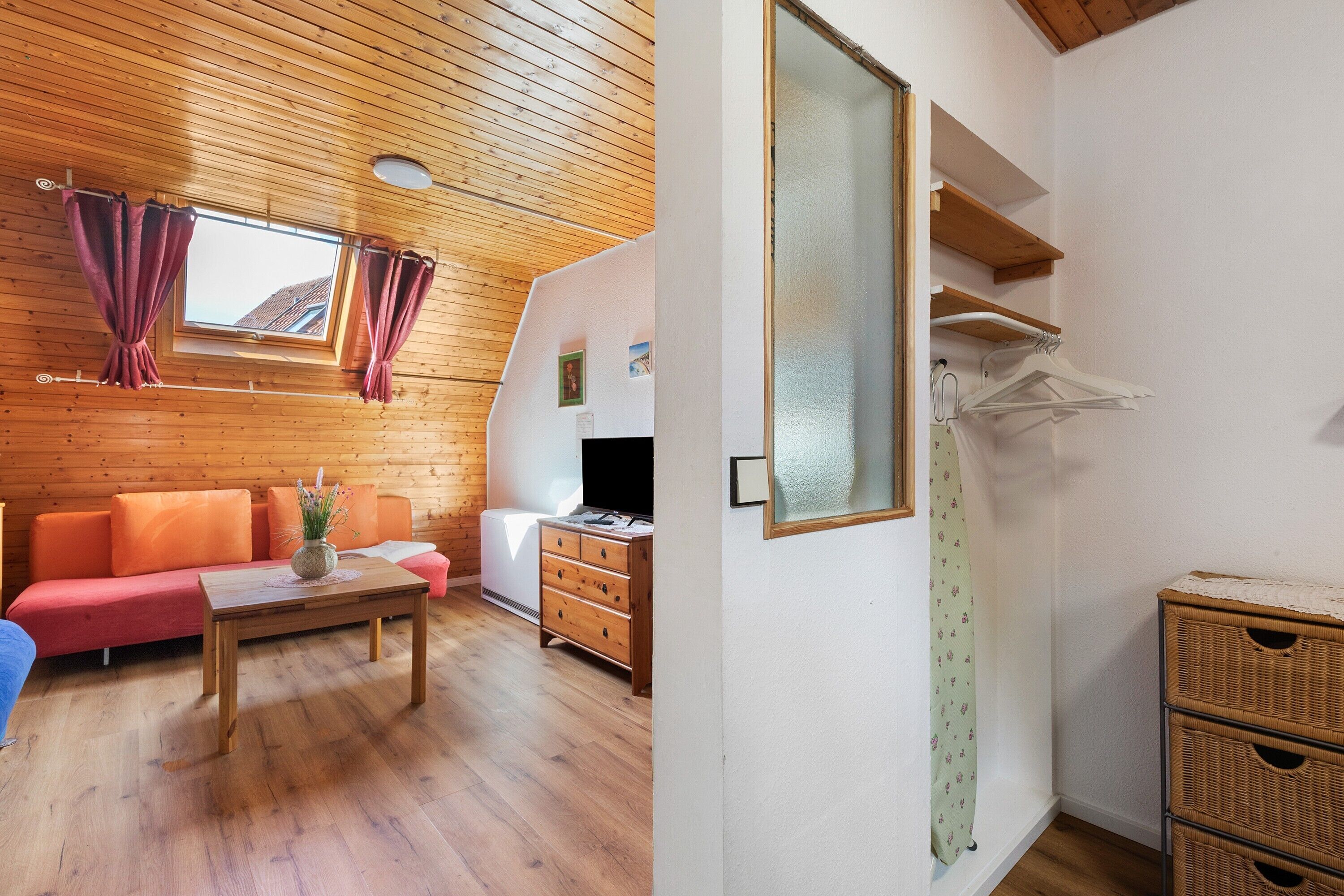 Una habitación con techo de madera, un sofá, una mesa, un aparador, un espejo y una ventana con cortinas.