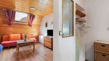 Una habitación con techo de madera, un sofá, una mesa, un aparador, un espejo y una ventana con cortinas.