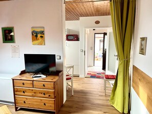 Une pièce comprenant une commode en bois, un téléviseur, un tableau et une porte donnant sur une autre pièce.