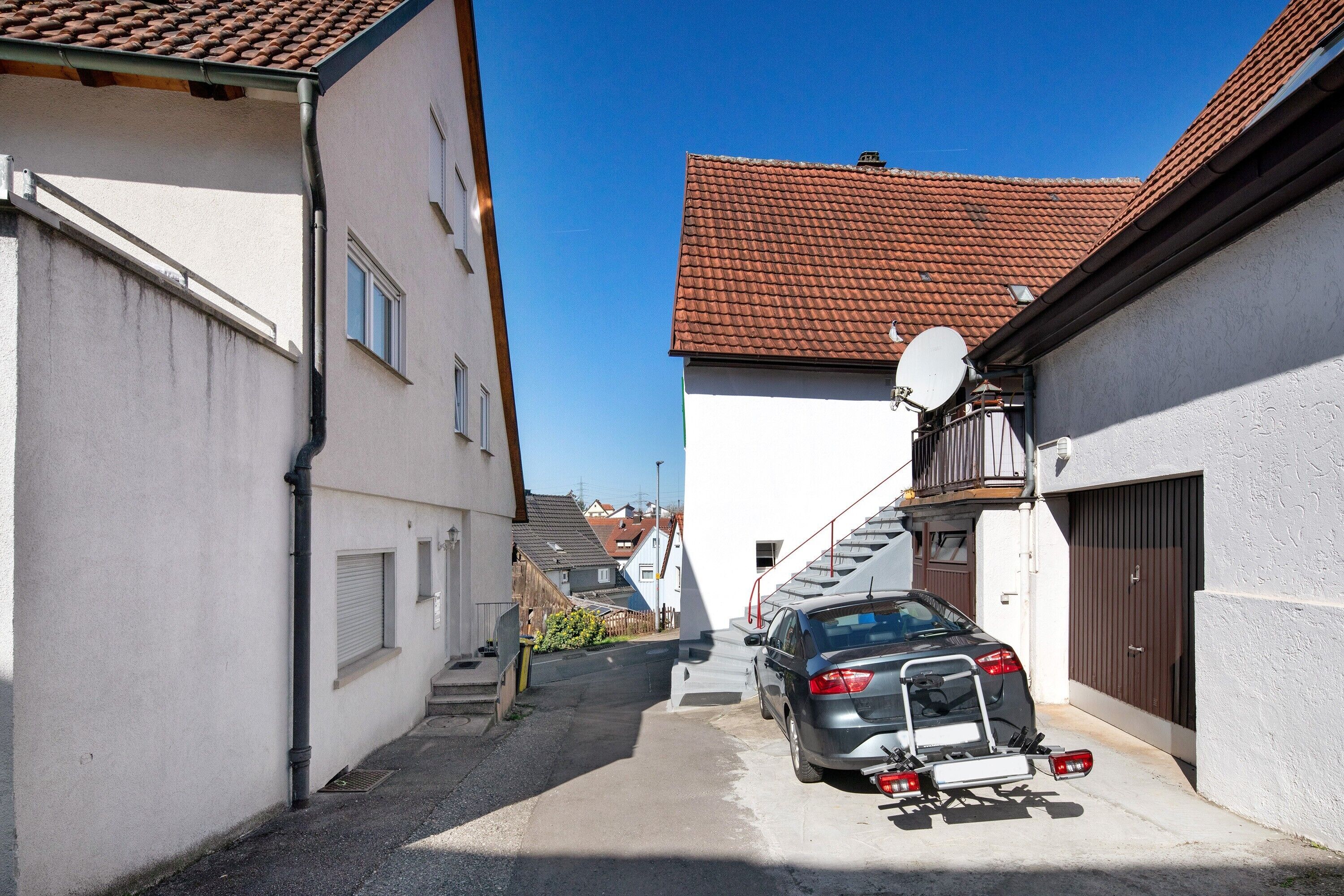 A narrow street with a parked car and a satellite dish on a building.