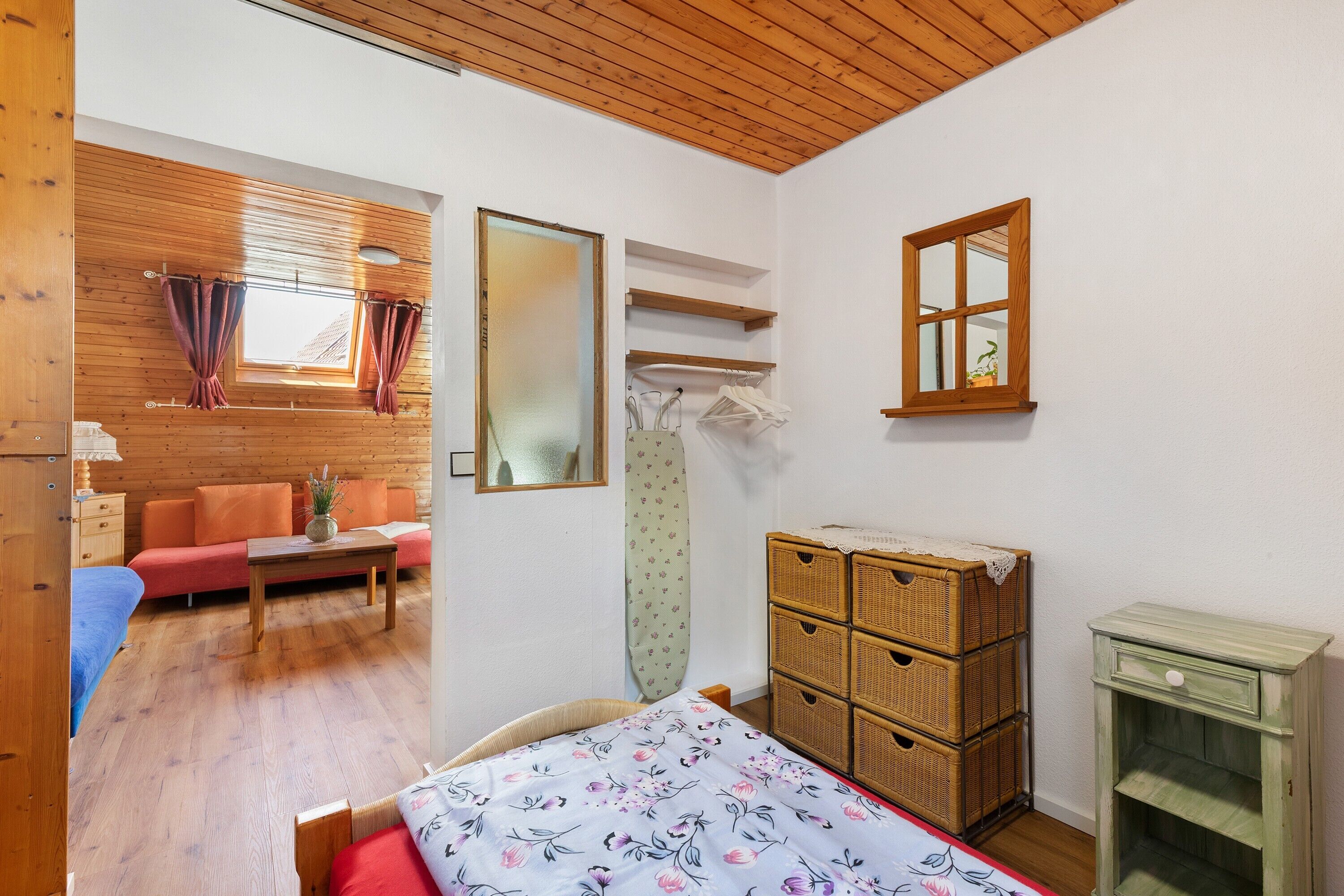 Habitació amb un llit, un taulell de fusta, una taula petita, un sofà, una finestra amb cortines i un mirall.