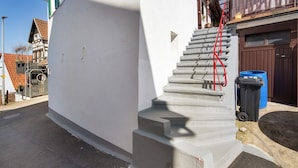 Una escalera de hormigón que lleva a una puerta, un cubo de basura azul y una puerta de garaje marrón.