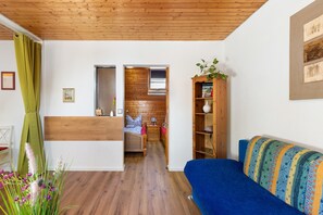 Une pièce avec un plafond en bois, un canapé bleu, une bibliothèque en bois et un lit avec une tête de lit en bois.